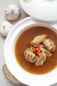 malaysian bak kut teh pork ribs soup - pork ribs, mushrooms and gogi at the middle with soup in the pot. Two pieces of garlic at side as decoration.